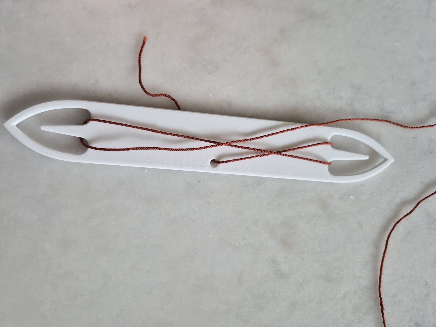 A weaving shuttle in plastic with openings and prongs, mirrored on both sides
