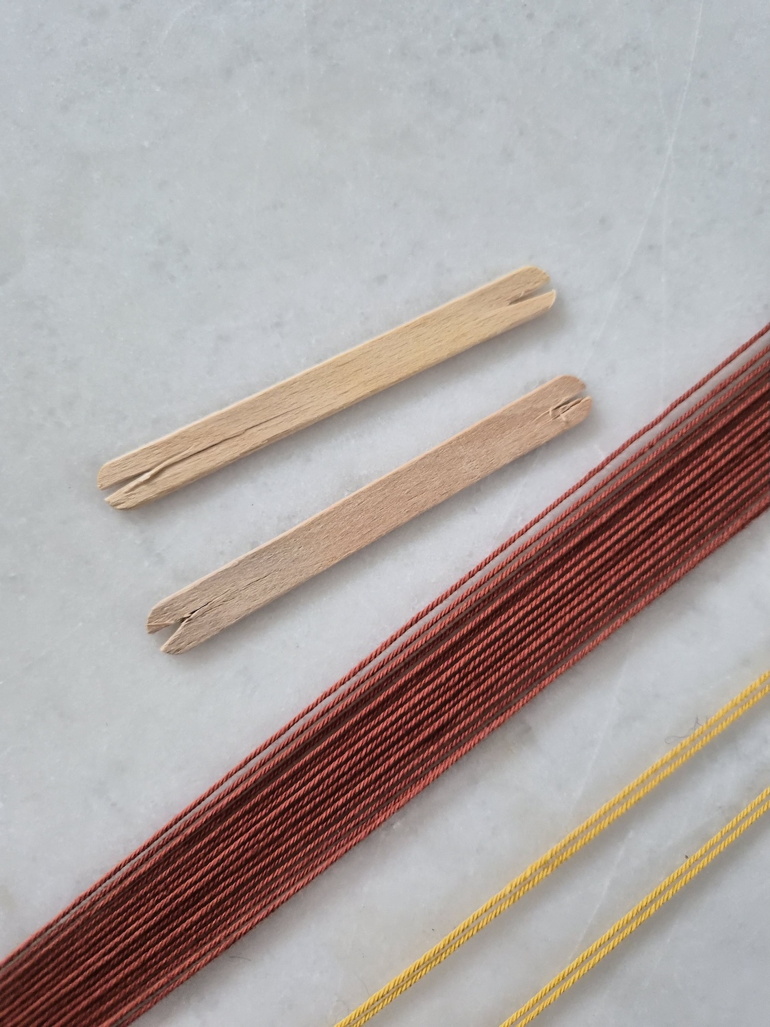 Yarn warped around a table top with two lolly sticks for shed sticks places next to the threads