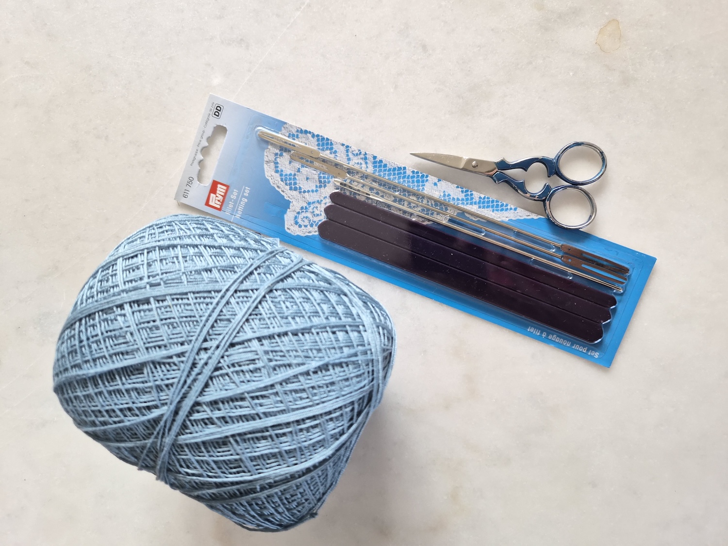 The tools to tie filet lace together with a scissor and a ball of yarn
