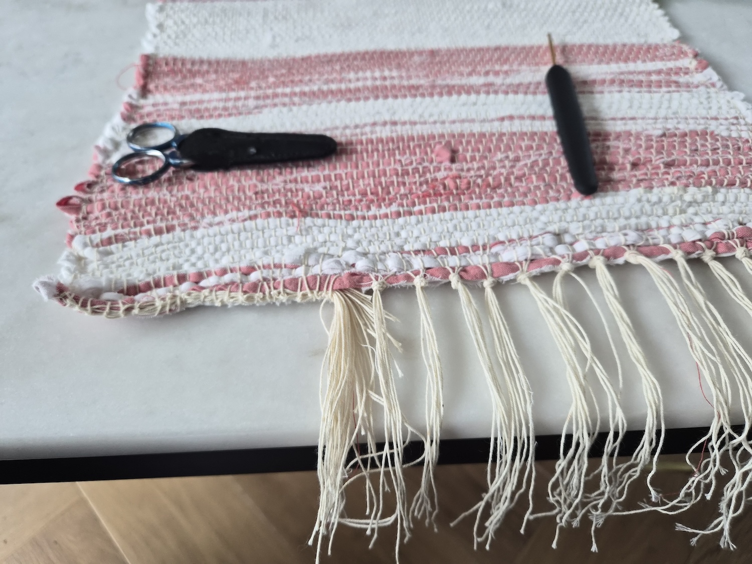 A table runner looking like a little rag rug on a marble table with ends in knots