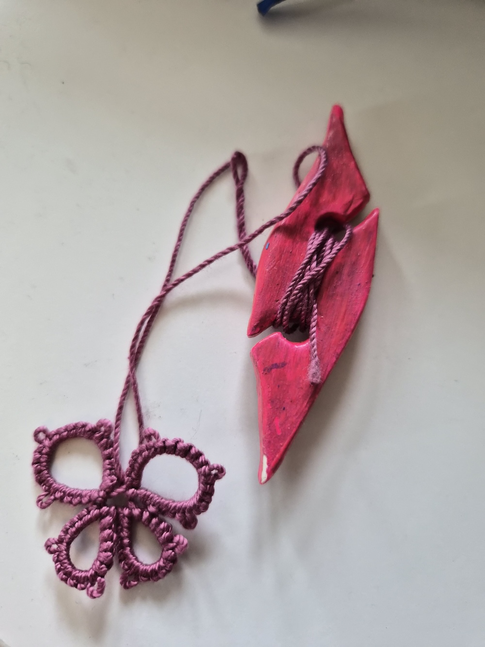 A clay tatting shuttle painted pink with a tatted butterfly next to it