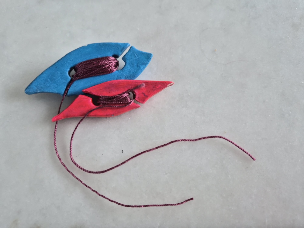 Two painted clay tatting shuttles wound with yarn