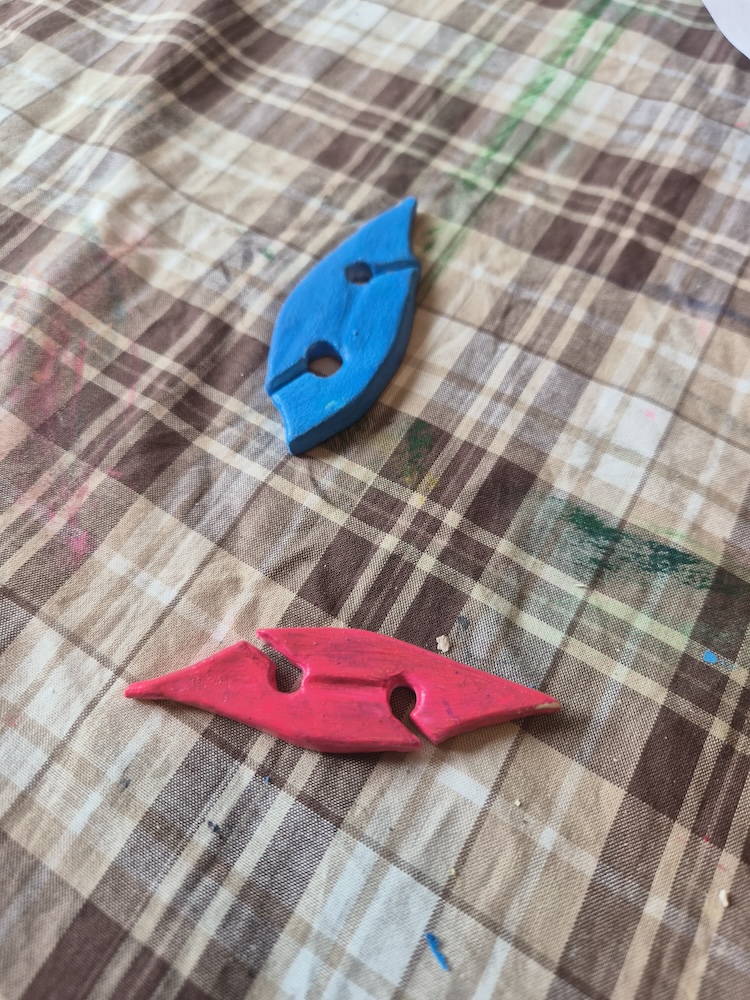 A picture of two tatting shuttleson a striped cloth with paint on them